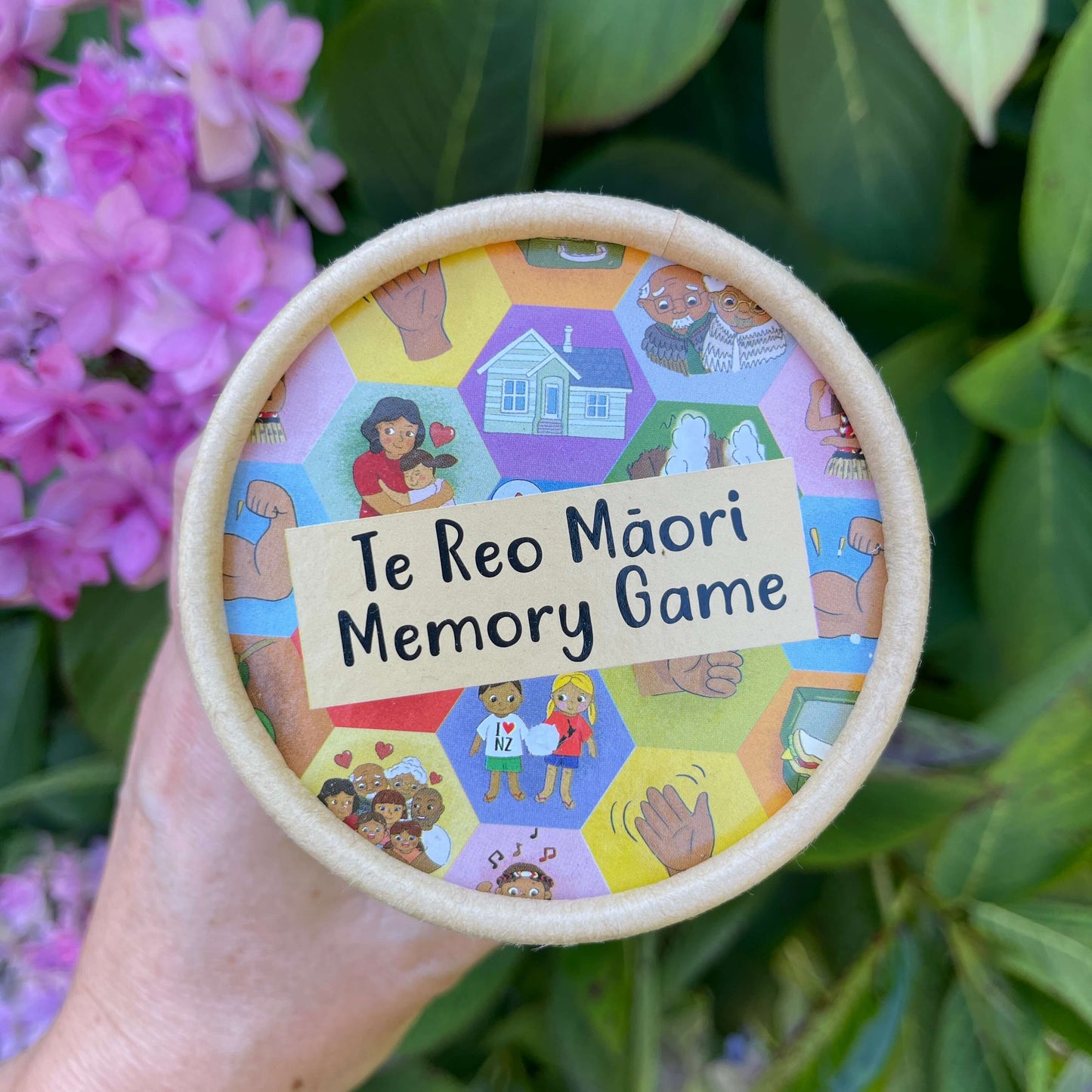 Women's hand holding cardboard tube with a Te Reo Maori Memory Game inside.