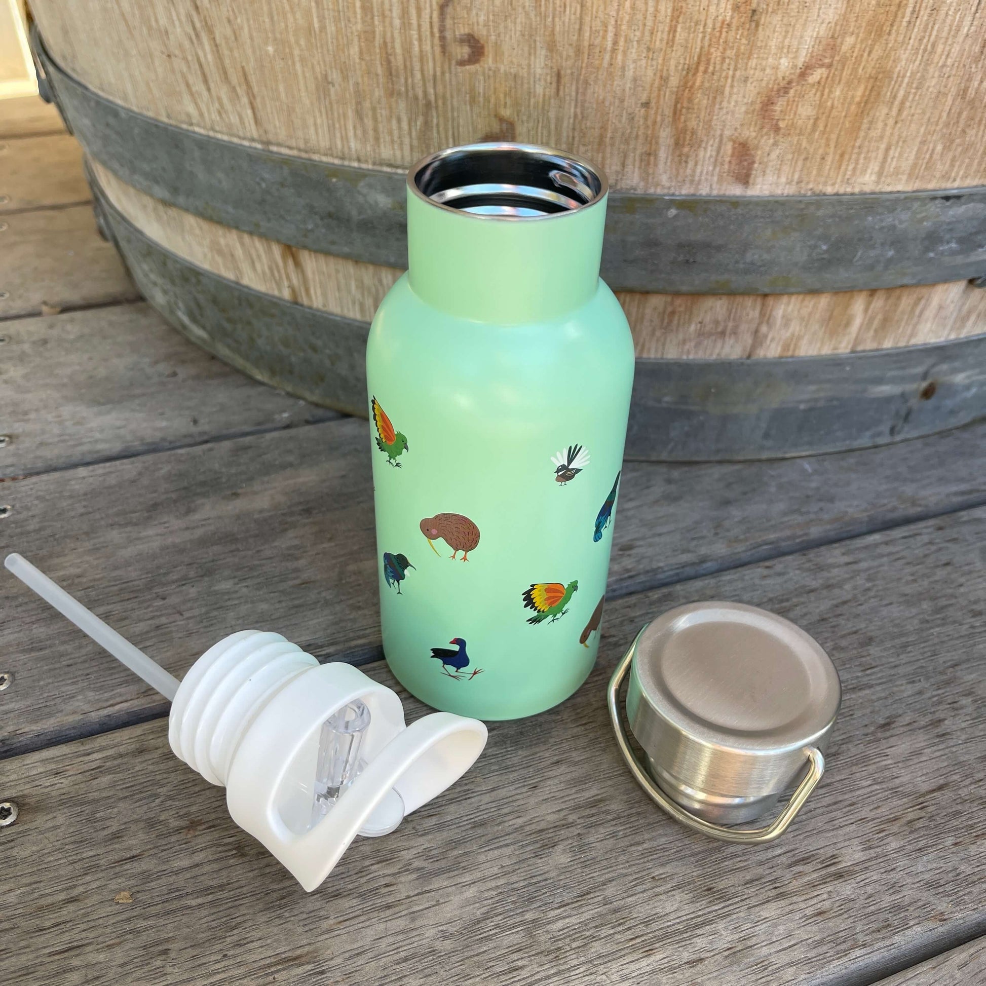 Small kids drink bottle with lid options removed and sitting next to it in mint green with New Zealand birds on it.