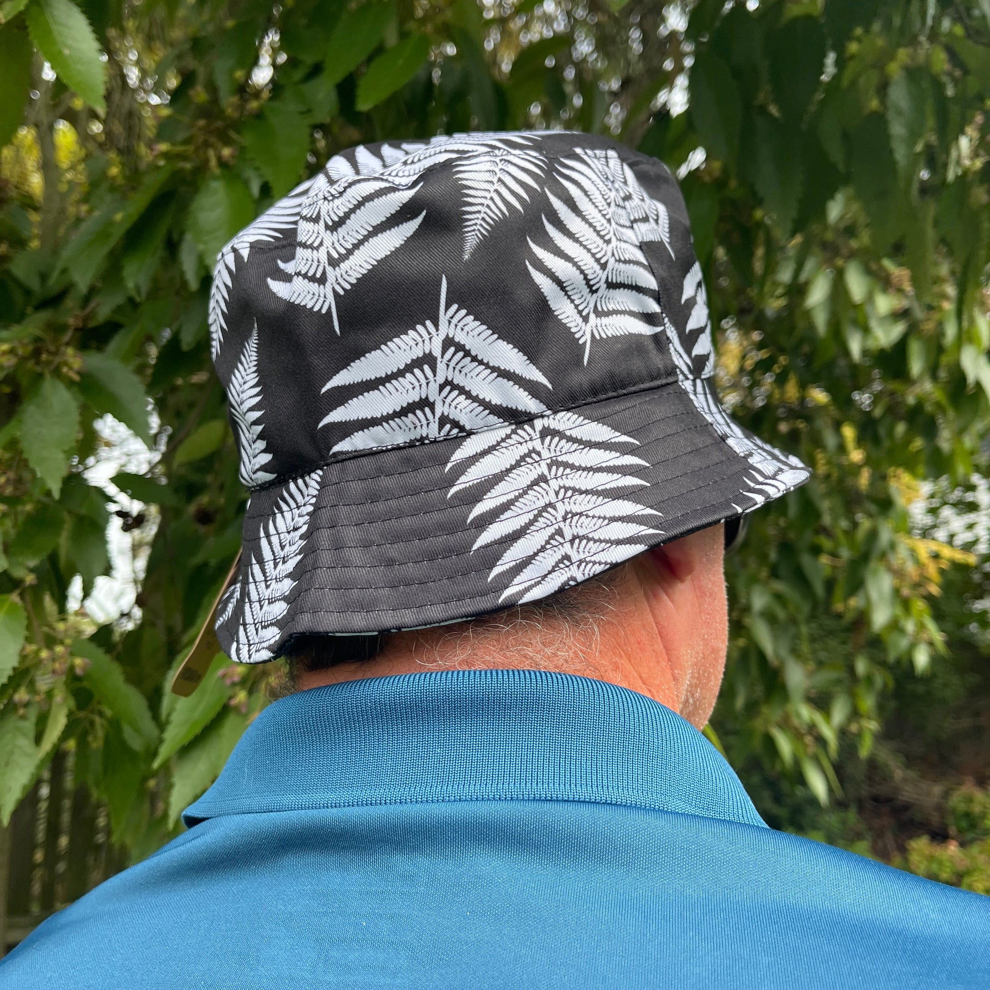 Back of mans head wearing a bucket hat in black with white ferns printed on it.