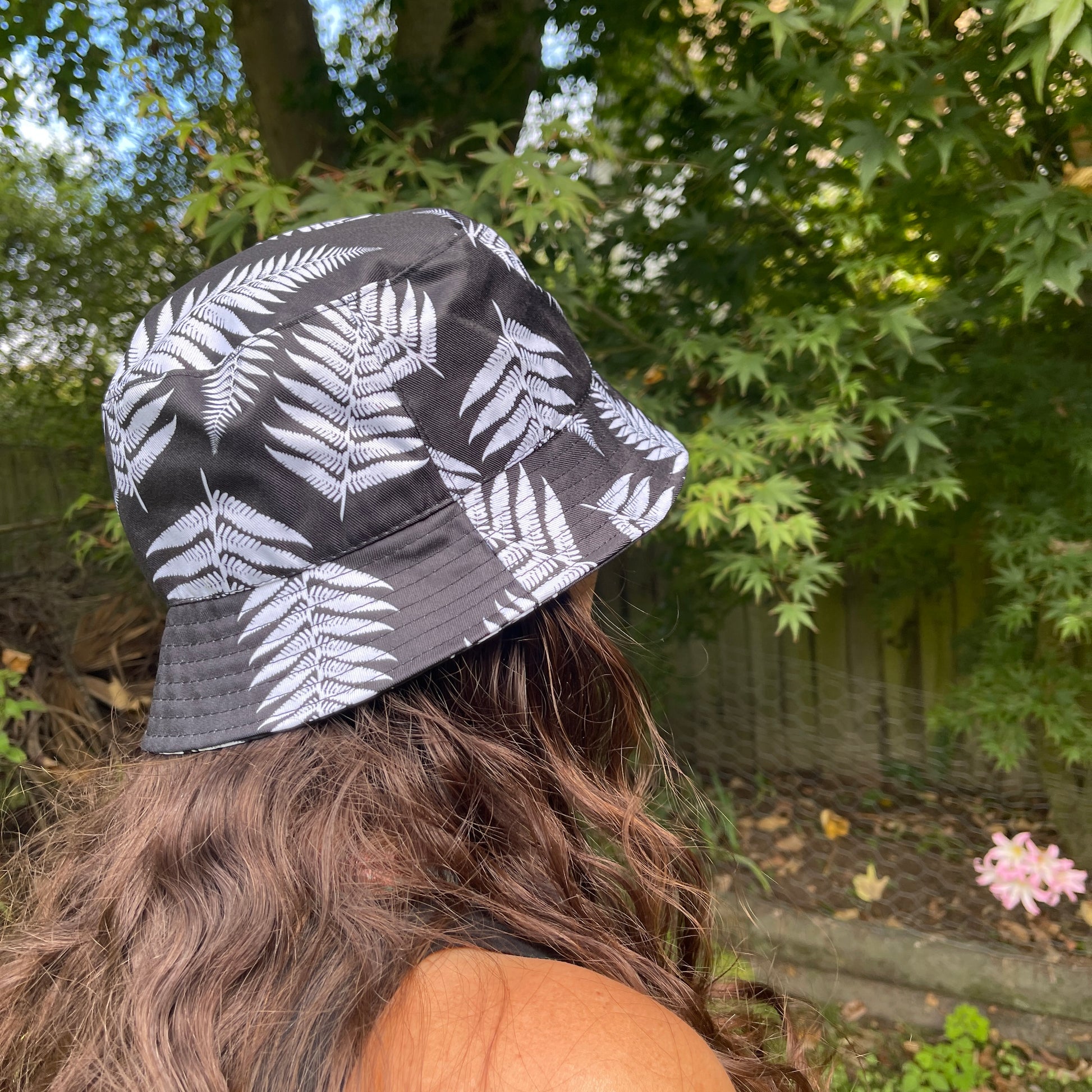 Side profile of a woman with long brown hair head wearing a bucket hat in black with white ferns printed on it.