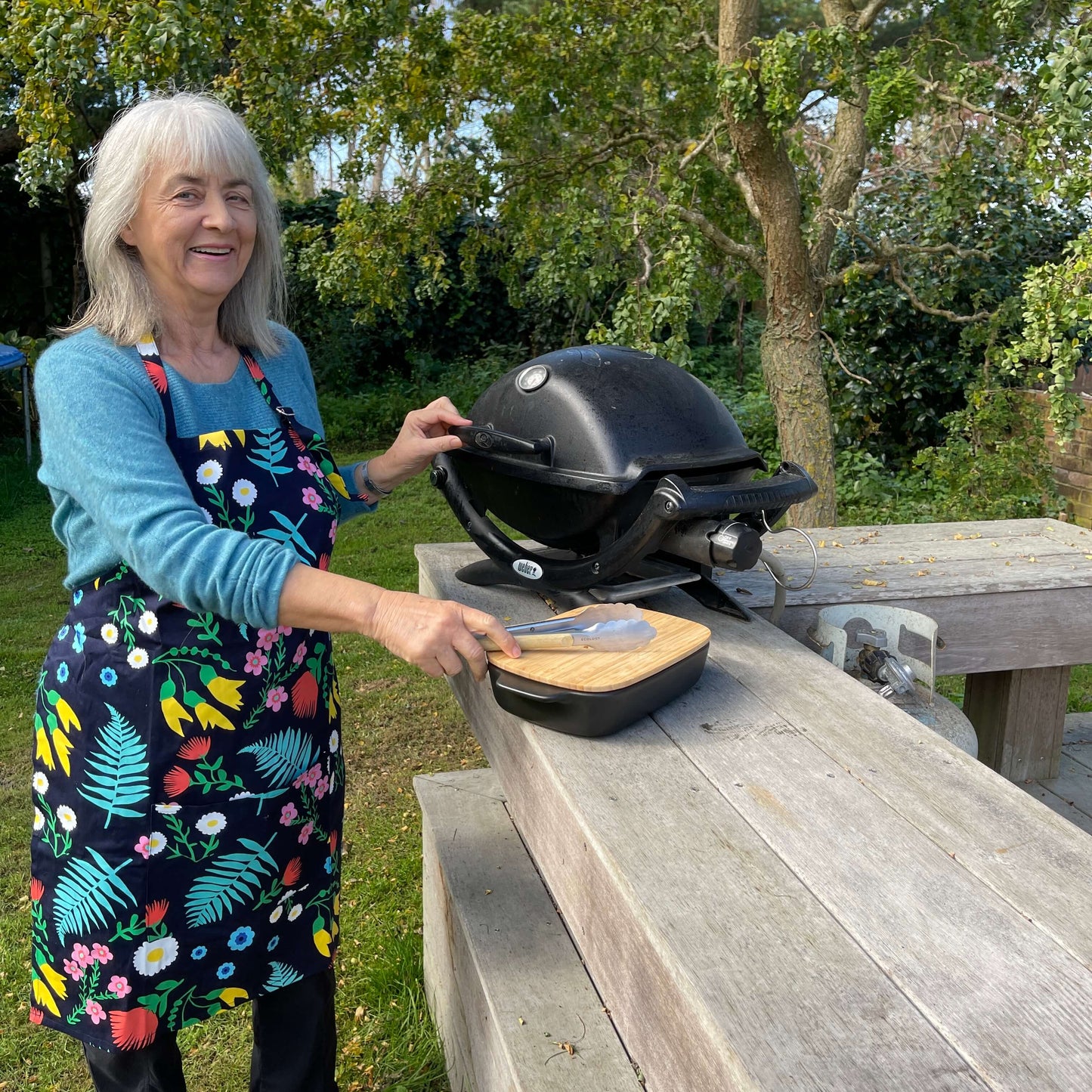 Woman wearing a navy blue and floral apron standing outside at a BBQ.