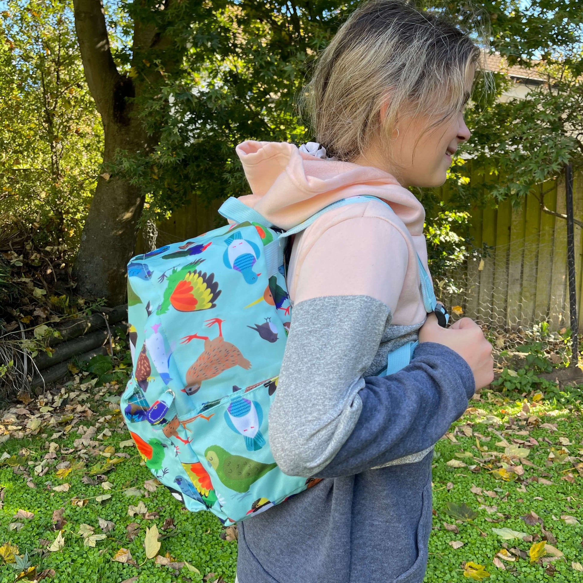 Child wearing a minty green backpack covered in bright prints of New Zealand birds.