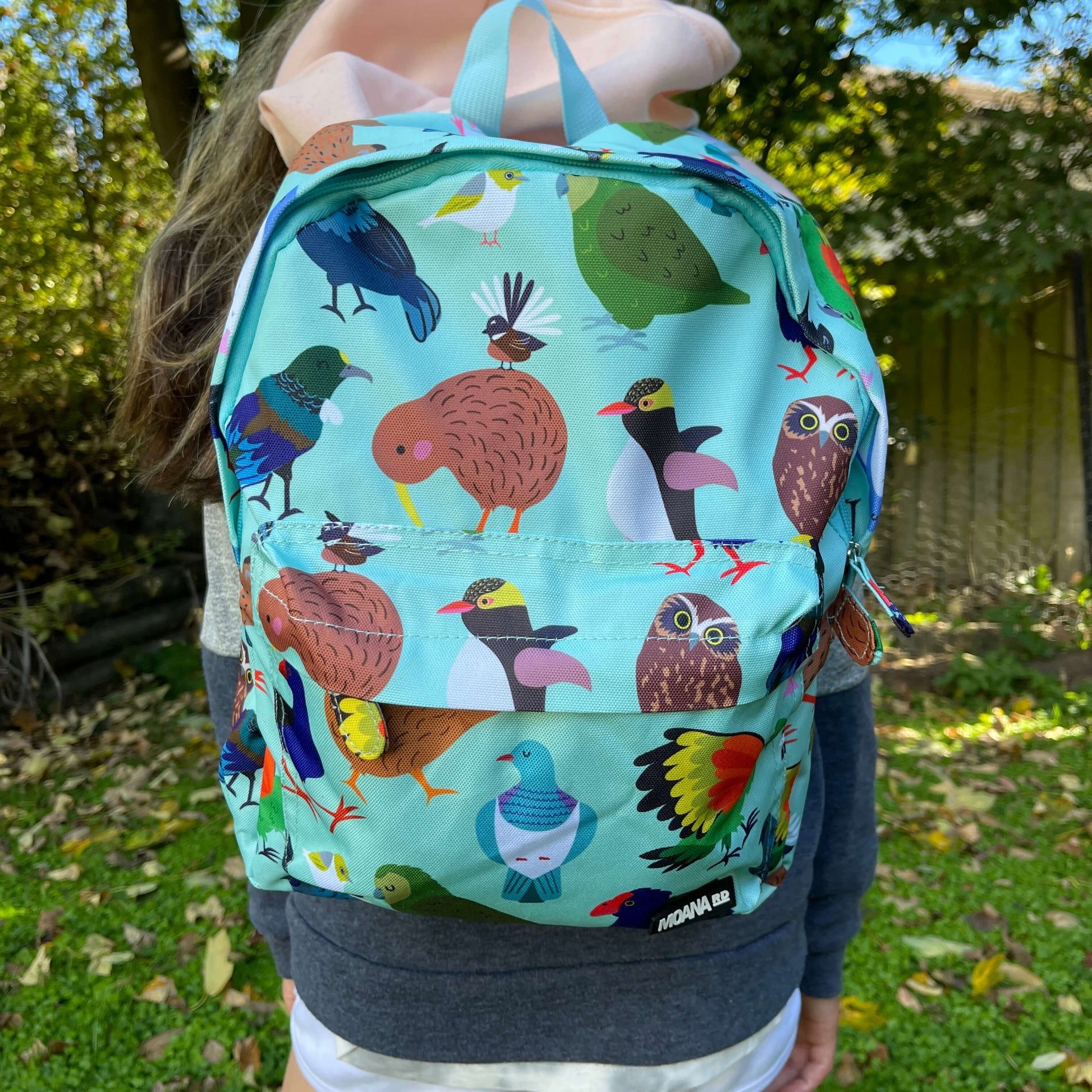 Child wearing a minty green backpack covered in bright prints of New Zealand birds.