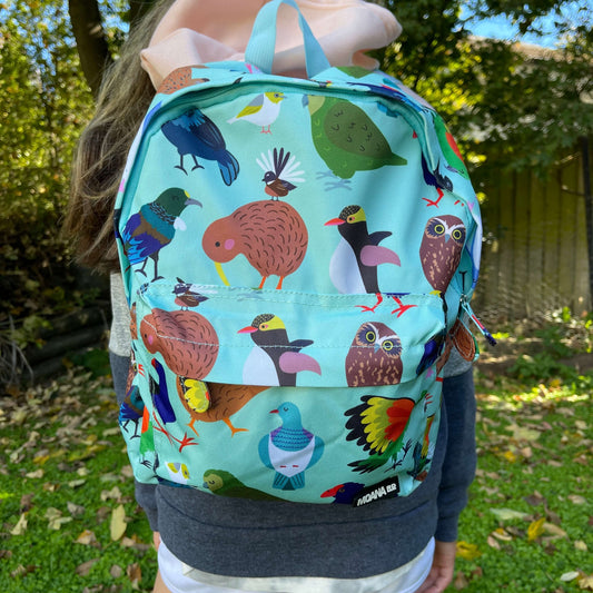 Child wearing a minty green backpack covered in bright prints of New Zealand birds.