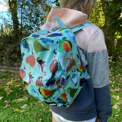 Child wearing a minty green backpack covered in bright prints of New Zealand birds.
