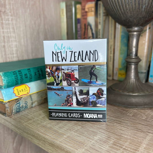 Pack of playing cards featuring scenes only found in New Zealand sitting on a book shelf.