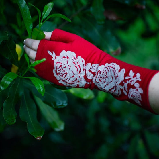 Beautiful Merino Wool glove on a womans hand touching a macadamia tree.Fingerless merino gloves in red with white rose print.
