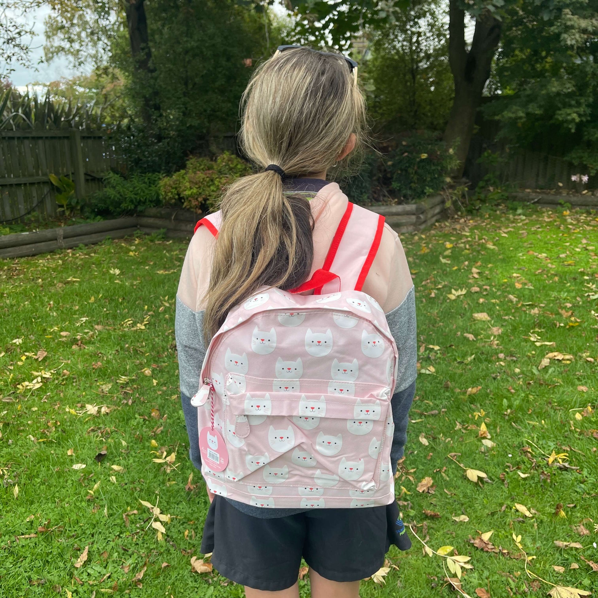 Girl wearing a pink backpack with white cat faces printed on it.