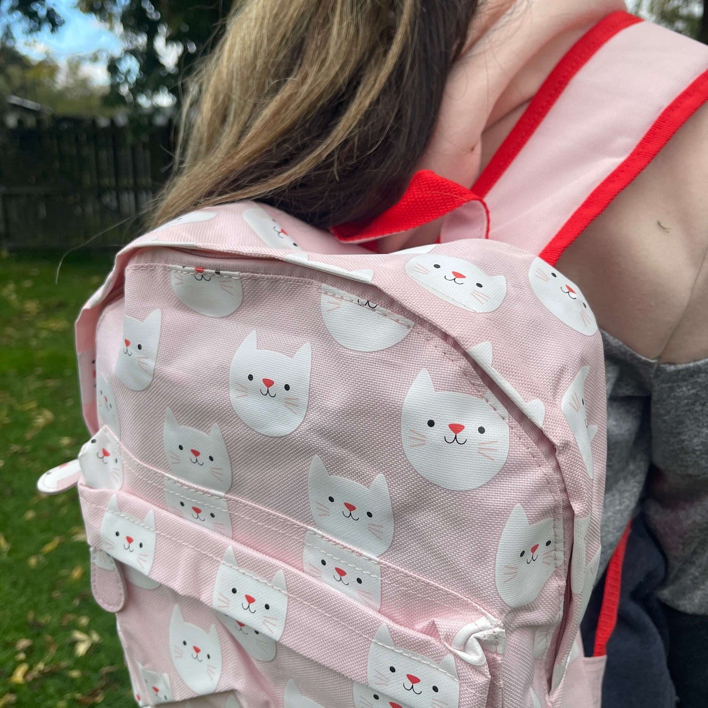 Girl wearing a pink backpack with white cat faces printed on it.