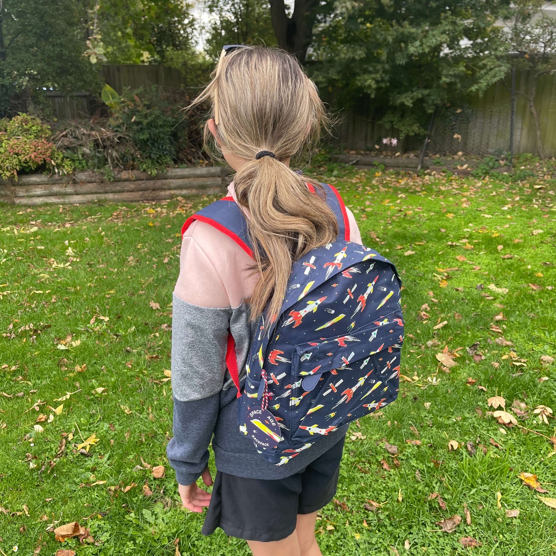 Girl wearing a navy blue backpack with rockets and space ships printed on it.