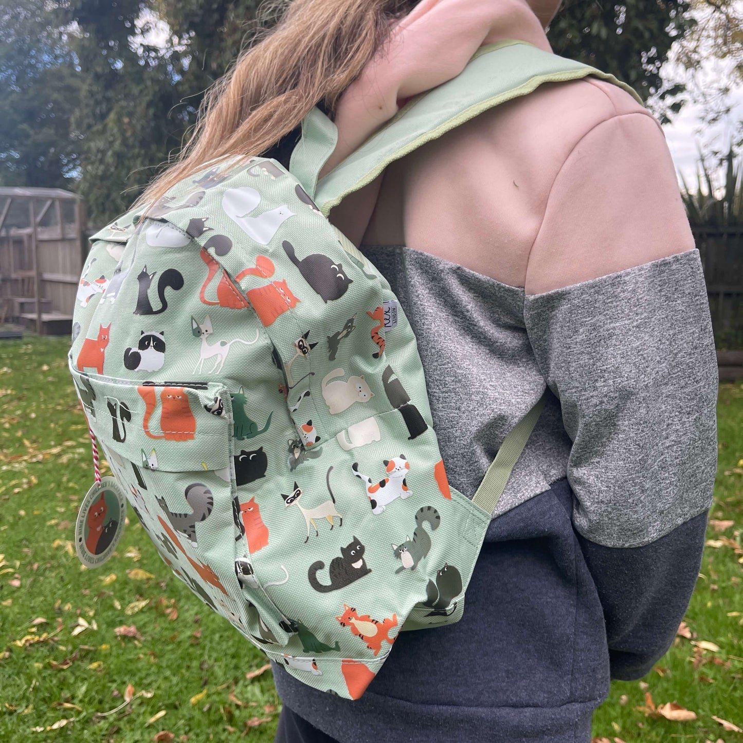 Girl wearing a mint green backpack with assorted coloured cats printed on it.