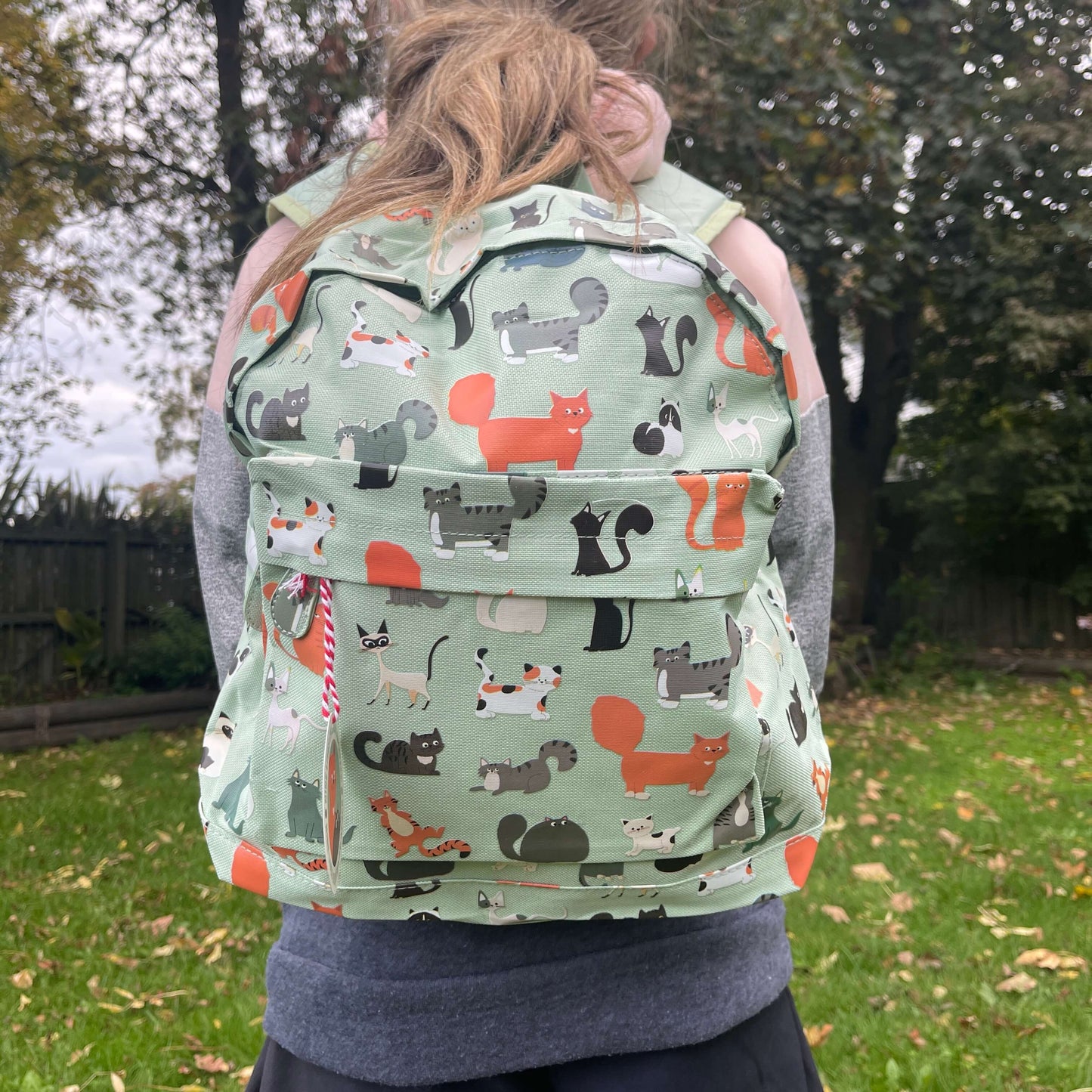 Girl wearing a mint green backpack with assorted coloured cats printed on it.