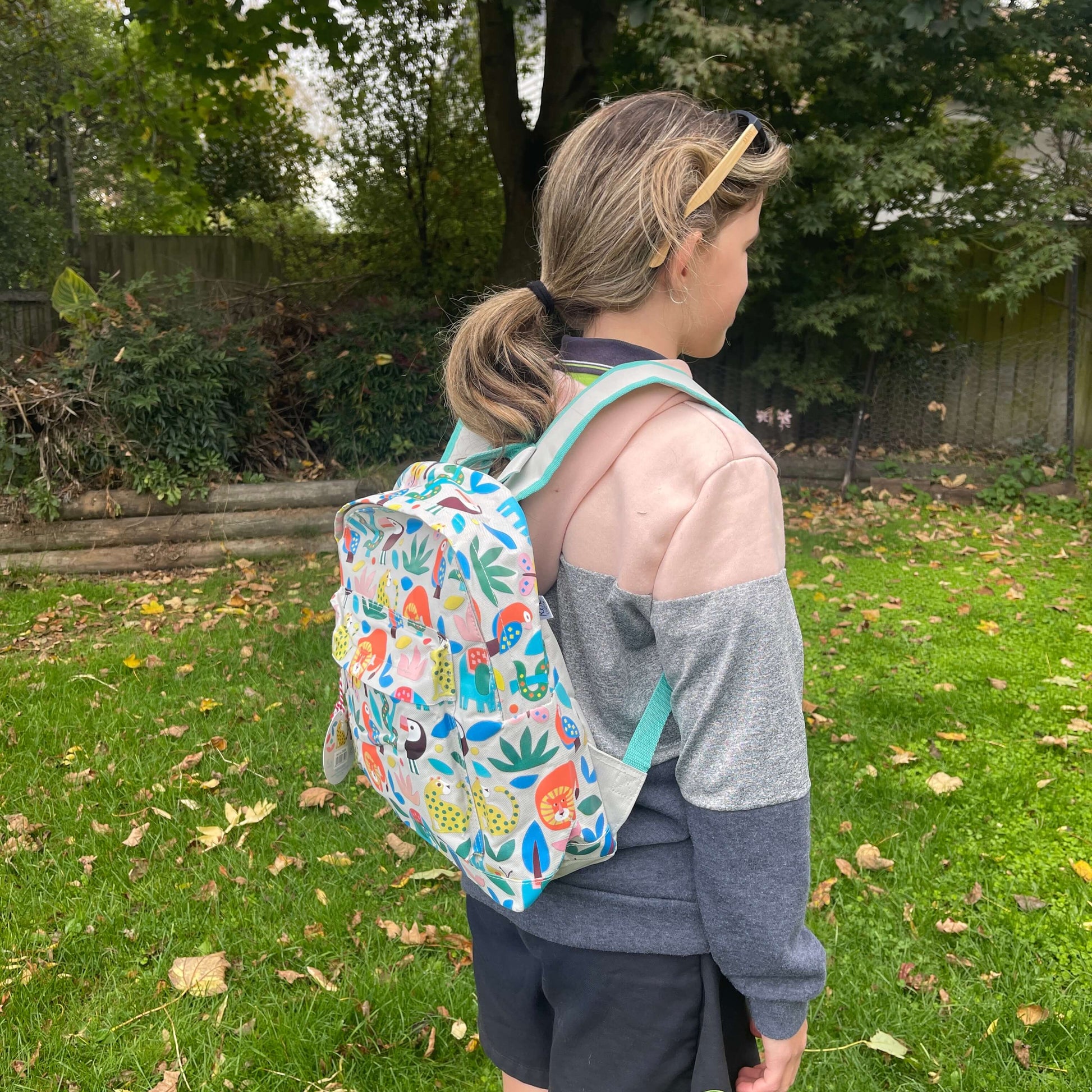 Girl wearing a backpack with bright jungle animals printed on it.
