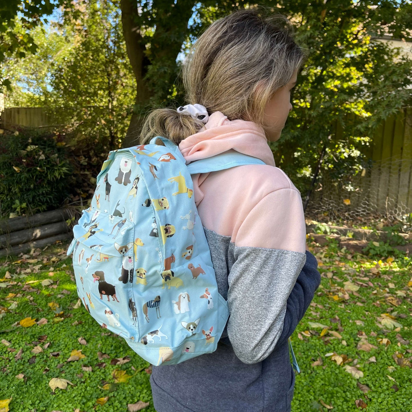 Girl wearing a pale blue backpack with various dogs printed on it.