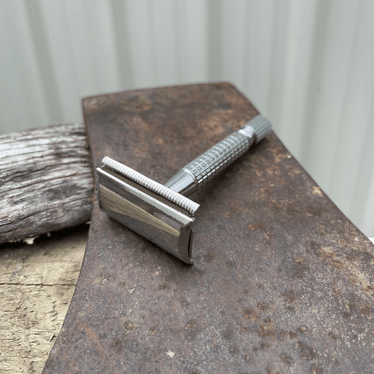 Metal safety razor sitting on the blade of an axe.