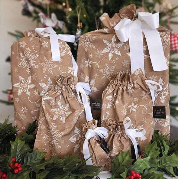 Reusable Christmas gift bags in beige with a white snowflake print and white satin ribbon.