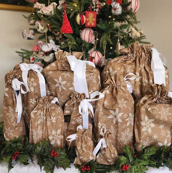 Reusable Christmas gift bags in beige with a white snowflake print and white satin ribbon.