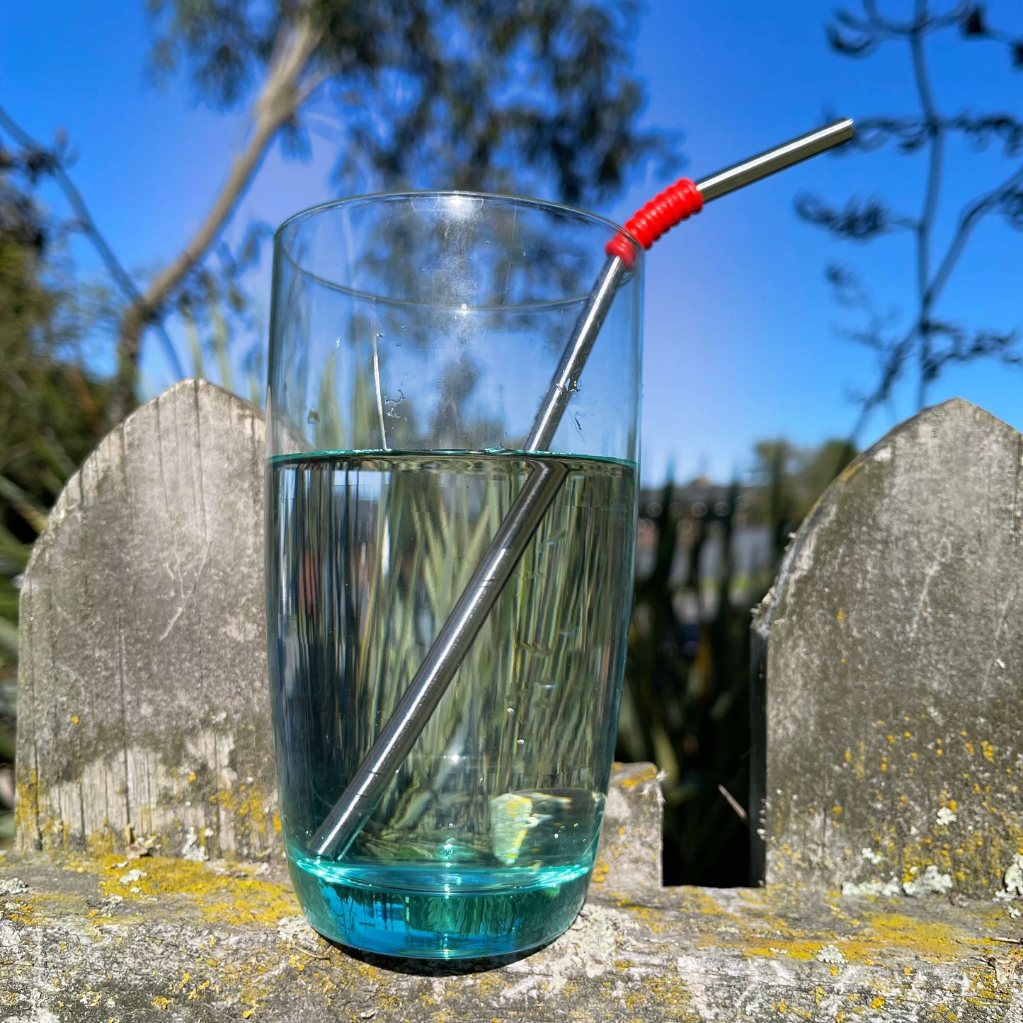 Blue water glass sitting on a fence filled with water and a stainless steel straw.