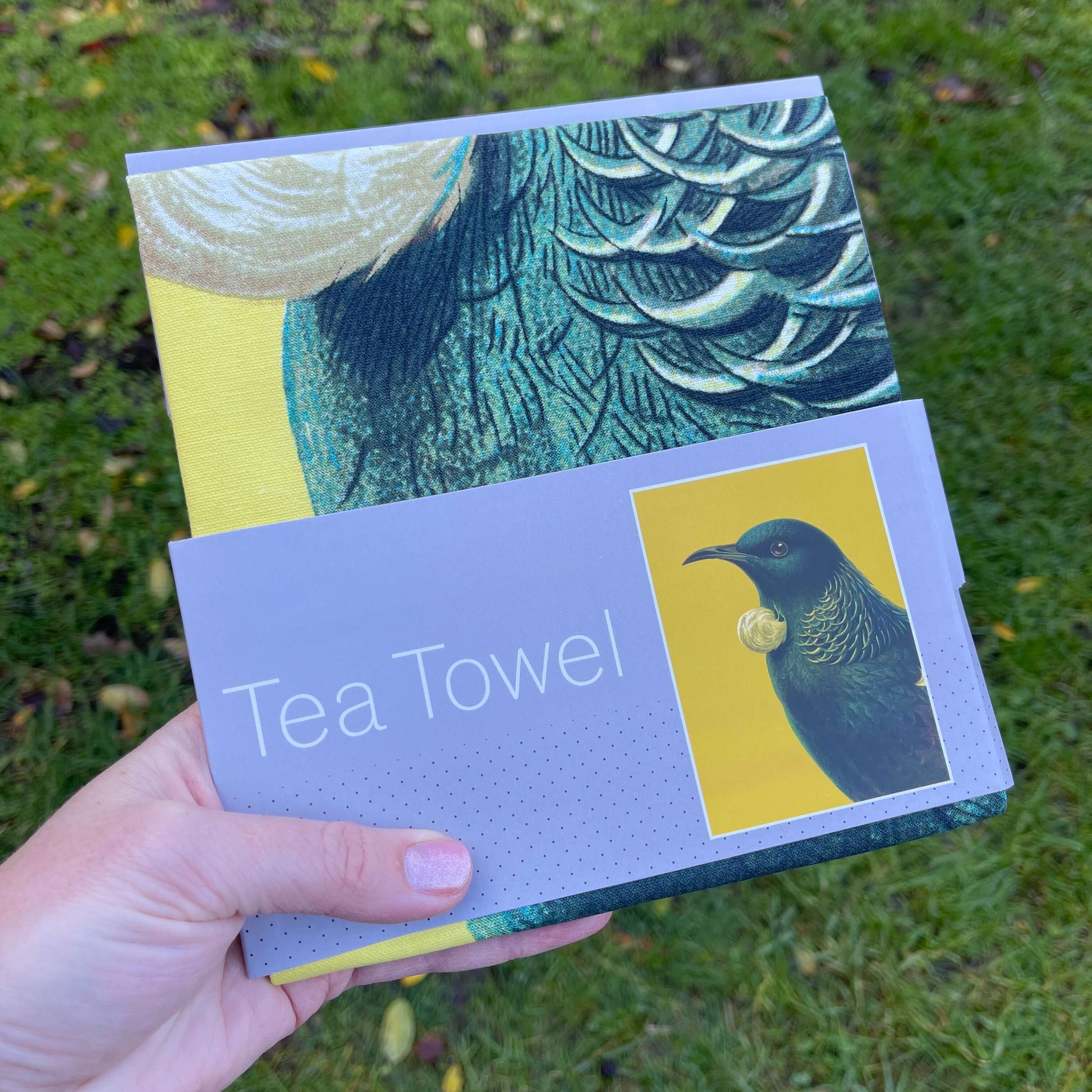 Bright yellow tea towel with a Tui on it.
