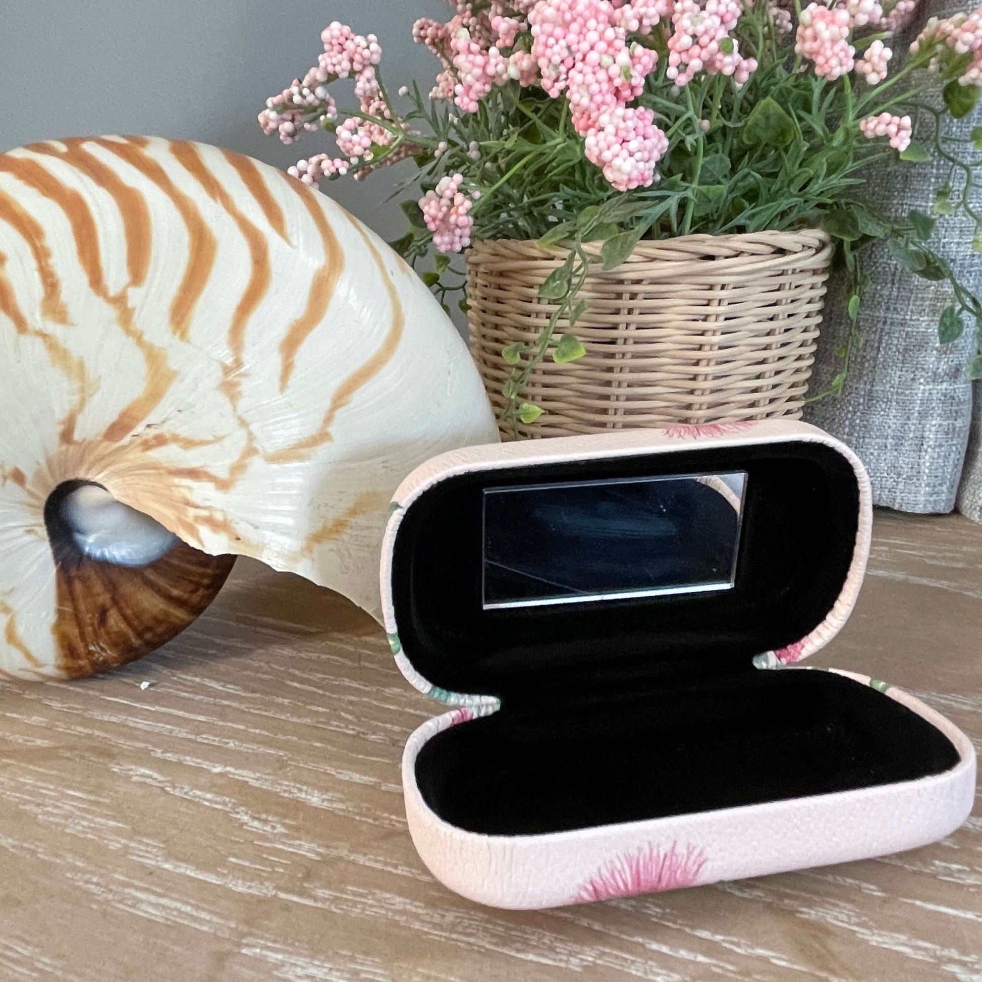  Small trinket case opened showing the mirror and black lining sitting on a table with a large shell and faux pot plant.