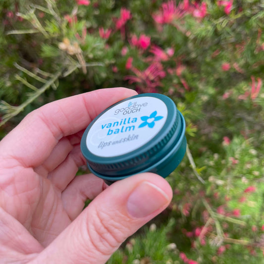 Persons hand holding a small tin of Vanilla Balm.