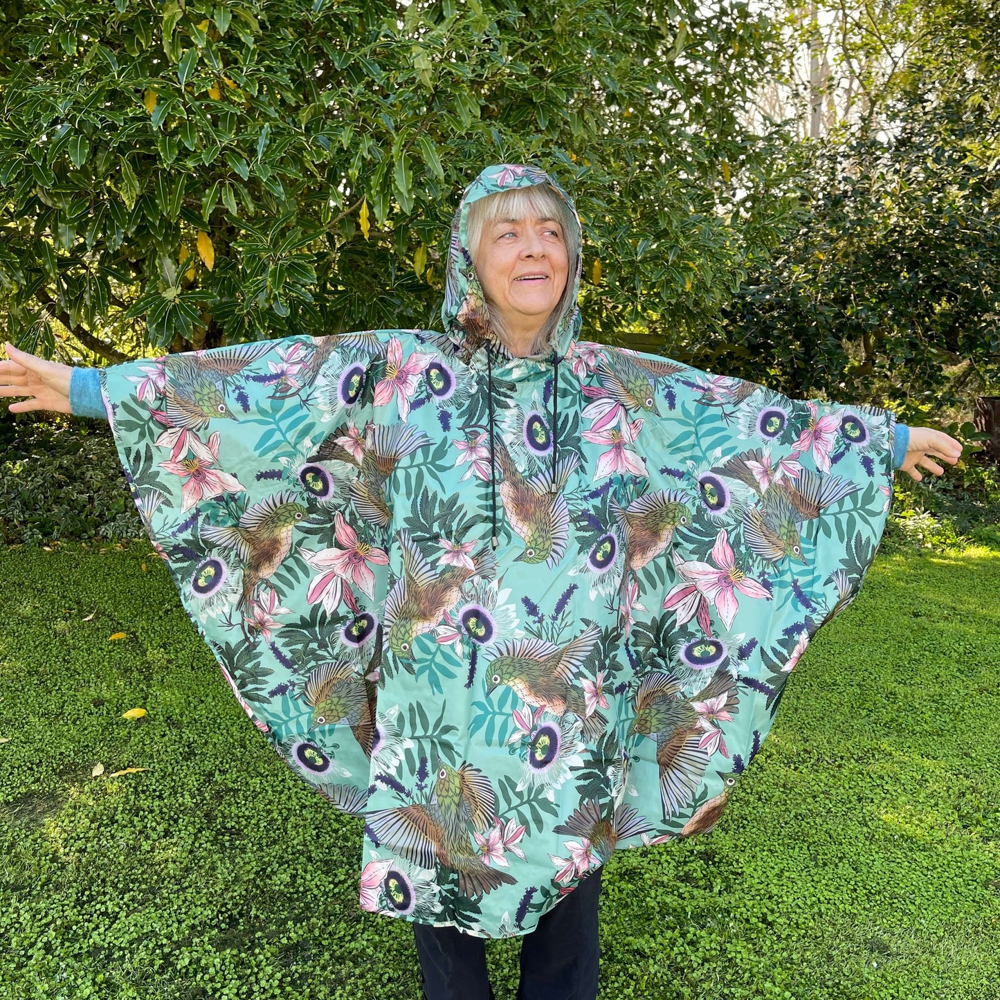 Woman wearing a rain poncho with birds and flower print on a light blue background.