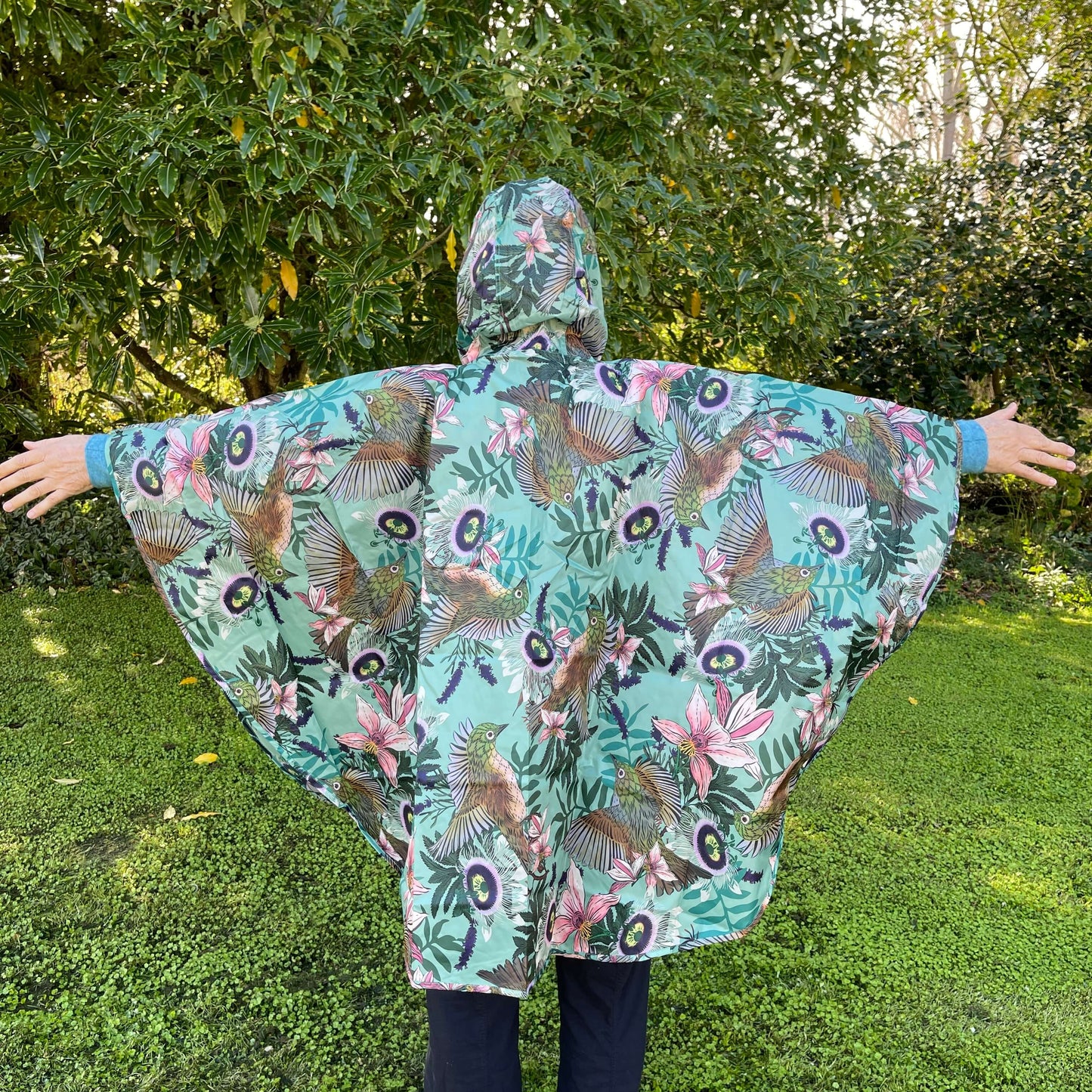 Woman wearing a rain poncho with birds and flower print on a light blue background.