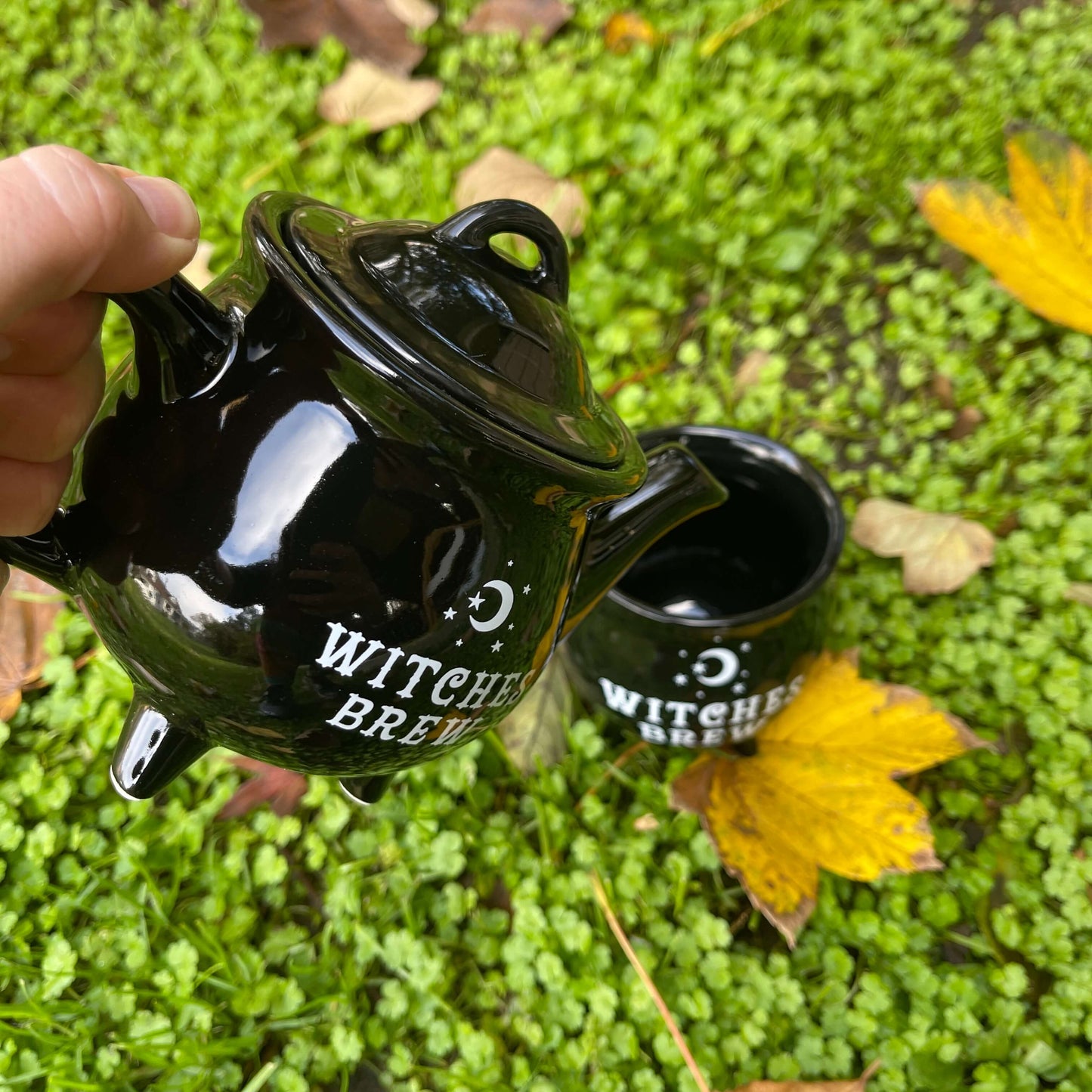 Black teapot with Witches Brew written on it in white pouring into a matching mug.