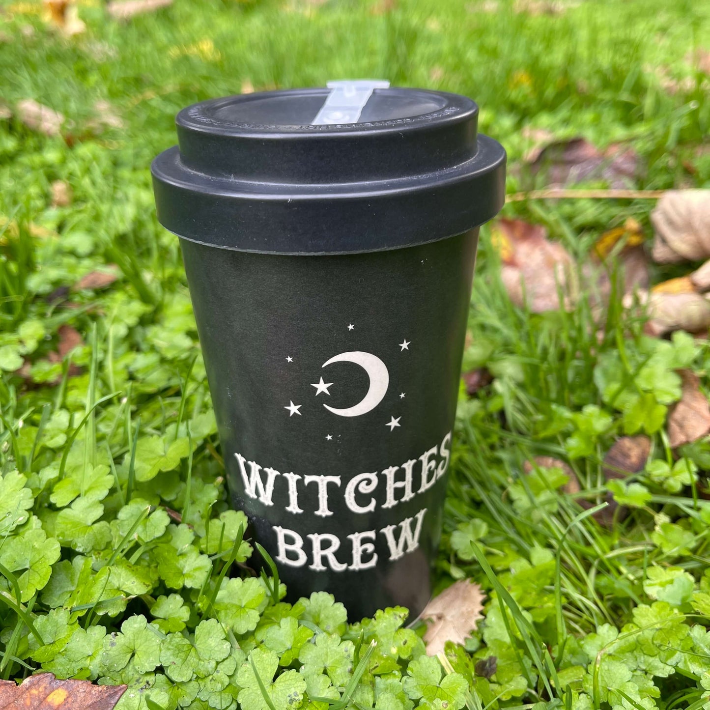 Black Bamboo Eco Travel Mug with white font saying "Witches Brew" on it sitting in the grass.