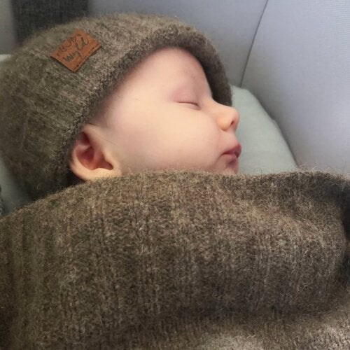 Baby asleep wrapped in a brown woolen blanket and wearing a matching hat.