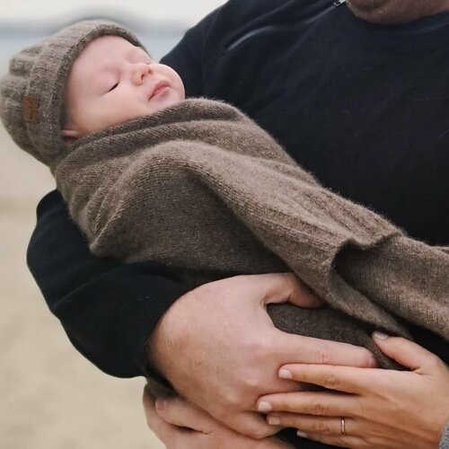 Baby in parents arms wrapped in a brown woolen blanket and wearing a matching hat.