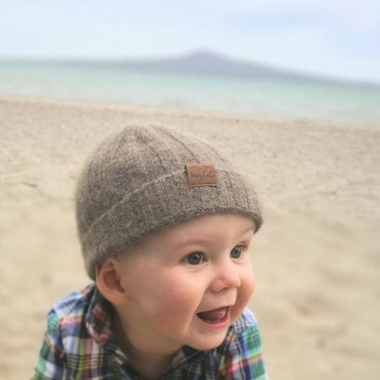 Baby on a beach wearing a brown knit beanie from Wyld.