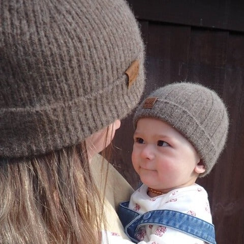 Women holding a baby, both wearing brown knit beanies from Wyld.