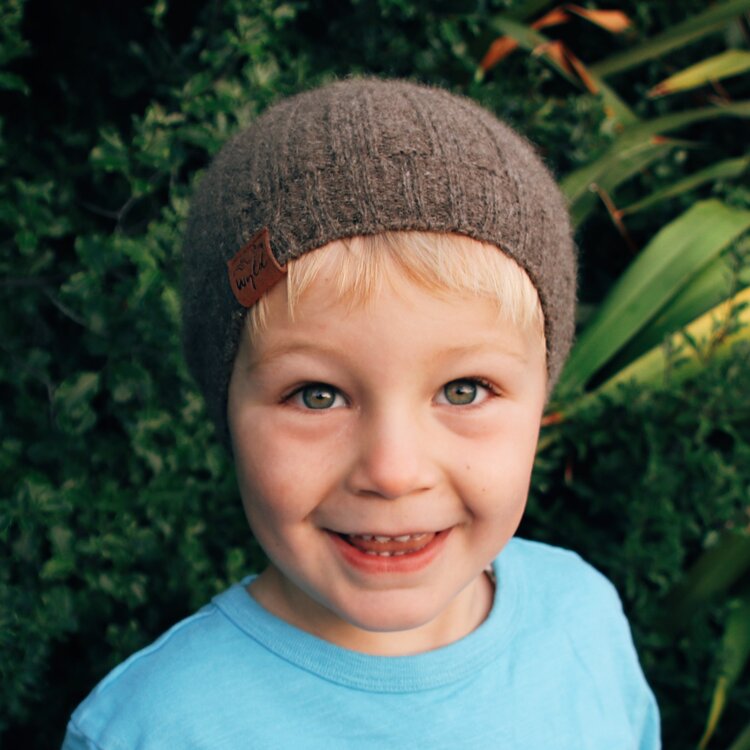 Toddler outside in front of bushes wearing a blue tee and a brown knit beanie from Wyld.