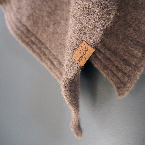 Corner of a brown woolen knit poncho against a grey wall.