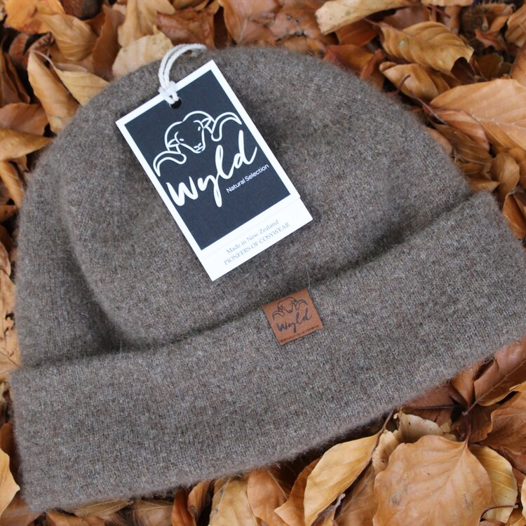 Wyld double layered wool beanie with leather tag sitting on a bed of leaves.
