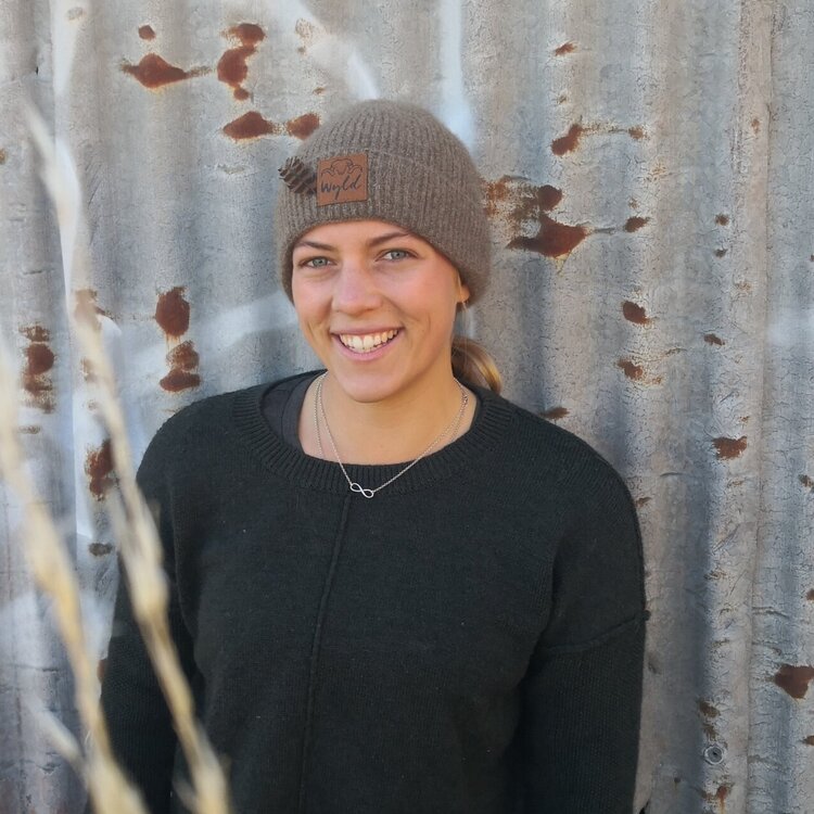 Women wearing a Wyld brown woolen beanie standing against a corrugated shed.