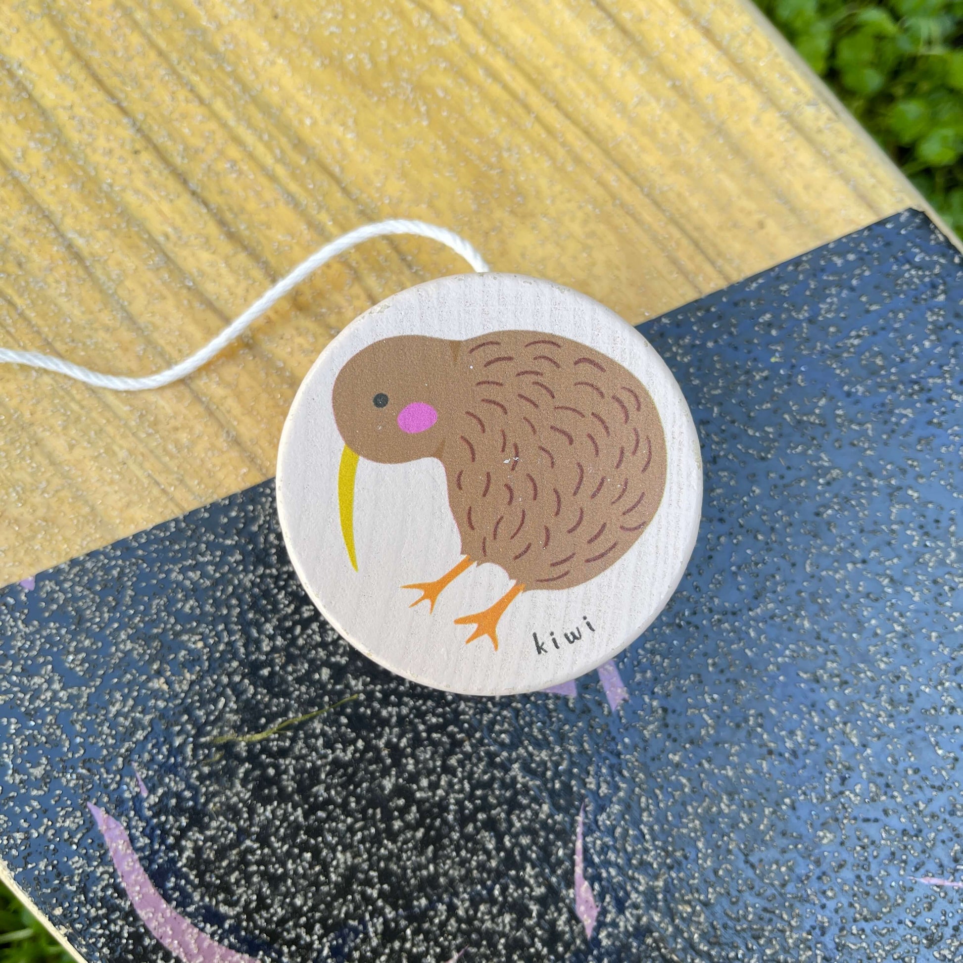 Pale pink wooden yoyo with a Kiwi bird painted on it sitting on a skateboard.