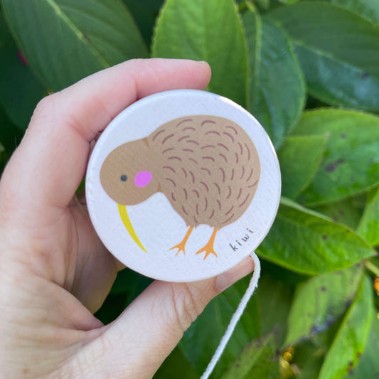 Womens hand holding a pale pink wooden yoyo with a Kiwi bird painted on it.