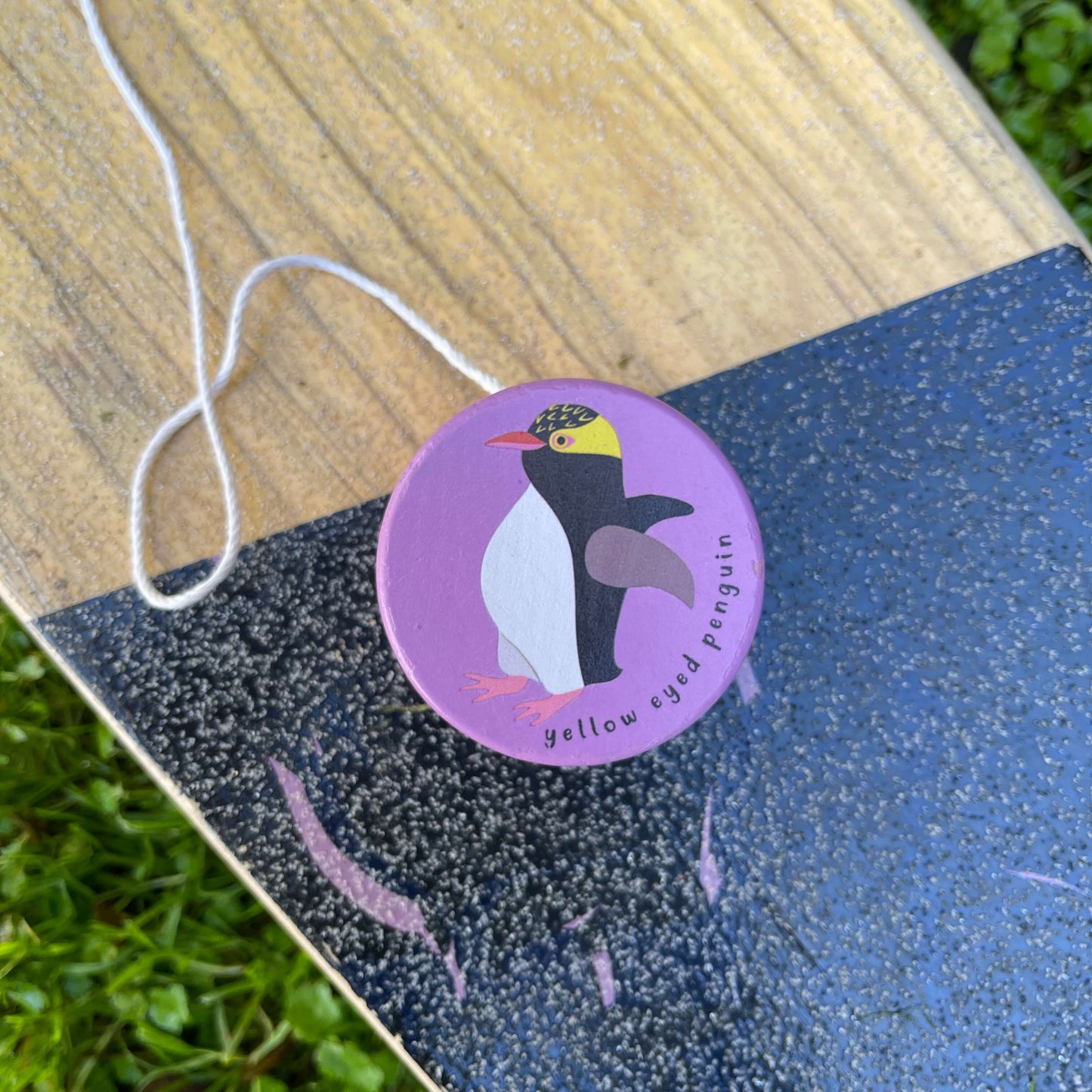 Purple wooden yoyo with a Yellow Eyed Penguin painted on it sitting on a skateboard.