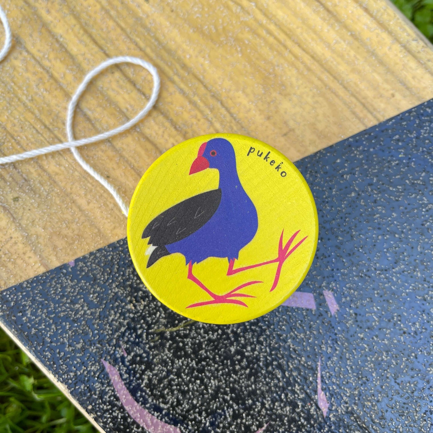 Bright yellow wooden yoyo with a Pukeko bird painted on it sitting on a skateboard.