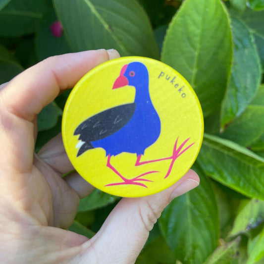 Womens hand holding a bright yellow wooden yoyo with a Pukeko painted on it,