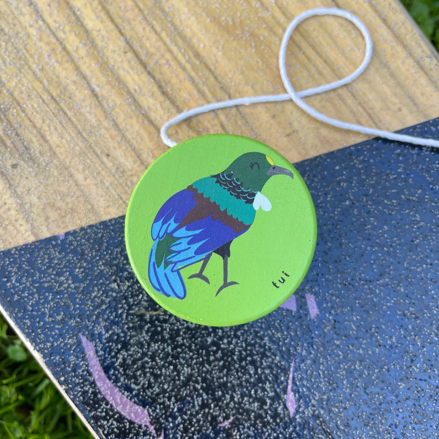 Bright green wooden yoyo with a Tui bird painted on it sitting on a skateboard.